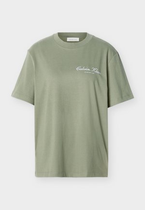 Ανοιχτό πράσινο ελιάς κοντομάνικο βαμβακερό T-shirt με στρογγυλή λαιμόκοψη και λευκό κείμενο «Calvin Klein Established 1968» στο αριστερό μέρος του στήθους.