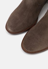 Bottes chevilles en daim gris foncé avec un bout pointu, dotées d'une semelle en cuir marron cousue et d'une texture lisse.