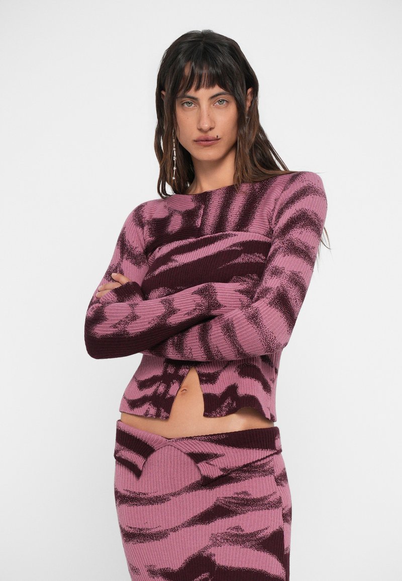 Stickad tvådelad set i rosa och vinröd med ett vågmönster. Tröjan har en rund halsringning och en framtill slits; kjolen har en figurnära silhuett.