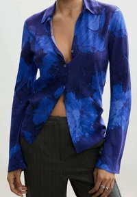 Blaues Kleidungsstück mit floralem Print, tiefem V-Ausschnitt und langen Ärmeln. Hergestellt aus weichem Stoff, mit Knopfverschluss und leicht taillierter Passform.