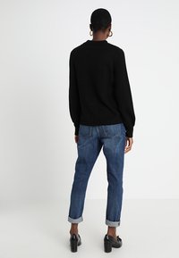 Czarny sweter z dzianiny z długimi rękawami, zestawiony z jasnoniebieskimi dżinsami z podwiniętymi nogawkami. Uzupełniony czarnymi butami na obcasie, tworzy swobodny, ale jednocześnie zorganizowany wygląd.