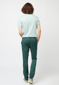 Lichtgroen overhemd met korte mouwen en donkergroene slim-fit broek, met details op de achterzak; gedragen met lichtgekleurde casual schoenen.