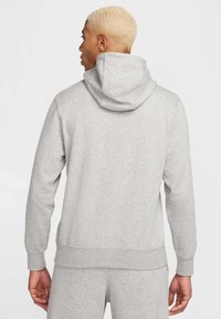 Vaaleanharmaa huppari, joka on valmistettu pehmeästä kankaasta, ja jossa on suuri huppu, pitkät hihat ja ribbaushelma. Yksinkertainen, koristeluton muotoilu.