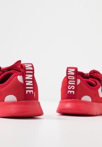 Baskets pour enfants rouges à pois blancs, chaque languette de talon portant l'inscription "MINNIE" et "MOUSE" en texte blanc.