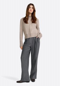 Maglione beige con collo alto e polsini a coste, abbinato a pantaloni grigi a gamba larga. Tessuto liscio e design semplice. Scarpe marroni.