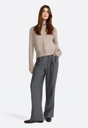 Maglione beige con collo alto e polsini a coste, abbinato a pantaloni grigi a gamba larga. Tessuto liscio e design semplice. Scarpe marroni.