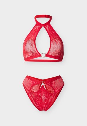 Rød blonder halterneck-bh og matchende trusse sæt med hjerteformede metalringe og subtile glitre detaljer på hvid baggrund.