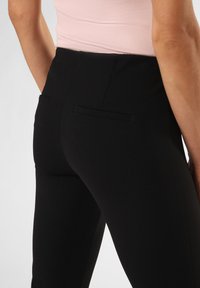 Zwarte textuur broek met twee achterzakken, voorzien van een slim fit en subtiel visgraatpatroon. De tailleband is iets verhoogd.