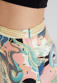 Jupe multicolore avec des motifs de dragon et de vagues. Tissu lisse avec une fermeture éclair et une taille rayée dans des tons pastel.