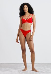Red lace bralette with adjustable straps, featuring a floral pattern and small bow detail. Paired with matching red high-cut panties.