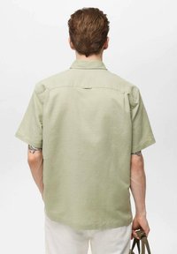 Camicia a maniche corte, di colore verde chiaro, con colletto classico, realizzata in lino e con dettagli sullo spacco posteriore. Presenta una vestibilità comoda e orlo piatto.