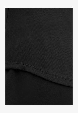 Zwarte sweatshirt met een geribbelde textuur, een ronde zoom en een klein logotag aan de zijkant. De stof lijkt zacht en rekbaar.