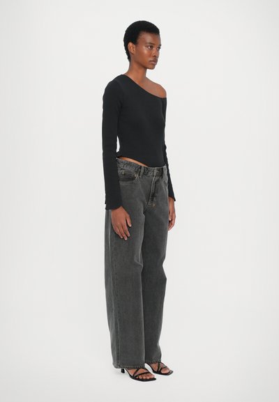 Top nero a maniche lunghe con scollatura asimmetrica, abbinato a jeans grigi scuri a vita alta e scarpe con tacco nere a strisce. Design minimalista.