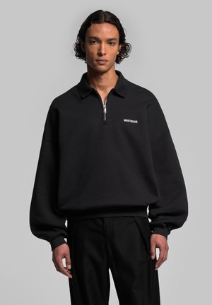 Black pullover sweatshirt with quarter-zip collar, featuring a white logo on the chest and relaxed fit. Made from textured fabric.