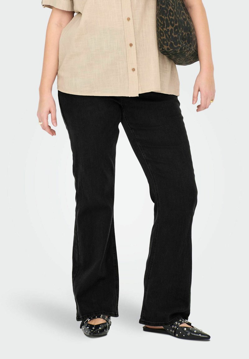 Jeans acampanados negros de tela de mezclilla, con una cintura de altura media. Combinados con una camisa de manga corta beige clara y bailarinas negras con tachuelas.