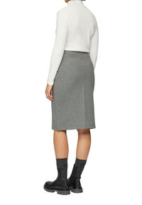 Jupe grise mi-longue en tissu doux, accompagnée d'un haut à manches longues blanc. Bottines noires à la cheville avec des chaussettes côtelées, montrant une silhouette épurée.