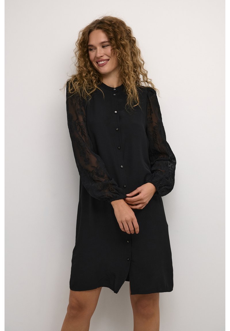 Black dress with long sheer embroidered sleeves, button front closure, and a slightly curved hem, made of lightweight fabric.