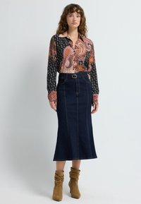 Bluzka z długim rękawem w wzór paisley na ciemnym tle z intensywnymi kolorami, w połączeniu z ciemnoniebieską spódnicą midi z paskiem i detalami w postaci szwów.