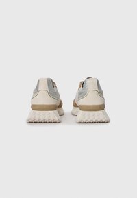 Beige and grey sneakers with textured suede, metallic accents, and a patterned rubber sole. Brightly colored brand logo on heel.