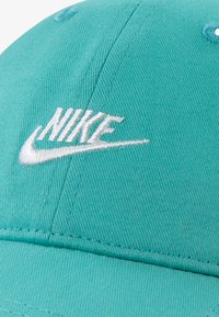 Tirkīza kokvilnas cepure ar baltu izšūtu "Nike" logotipu un gludu tekstūru, ar redzamām šuvēm un izliekta brīma dizainu.