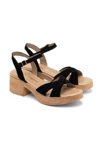 Czarne zamszowe sandały z grubą, teksturowaną beżową podeszwą. Posiadają krzyżujące się pasy oraz regulowane paski wokół kostki z metalową klamrą.