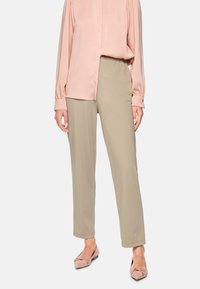 Beige trousers with a straight cut, paired with a light pink satin blouse. Pink flats feature a decorative bow. Smooth textures throughout.