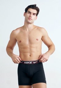 Crne Nike bokserice s bordo pojasom na kojem je prikazan Nike logo u bijeloj boji. Glatka tekstura i prilagođen dizajn.
