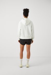 Sudadera blanca con capucha hecha de material suave, combinada con pantalones cortos negros, con puños y dobladillo acanalados, detalle del logo visible en la parte trasera.