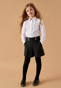 Bela srajca s čipkastimi detajli, črne hlače z visokim pasom z zlatimi gumbi, črne knee-high nogavice in črni čevlji z okrasno pentljo.