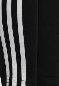 Pantalones deportivos negros con tres franjas verticales blancas a lo largo del costado. Fabricados en tela acanalada con un diseño ajustado y cintura elástica.