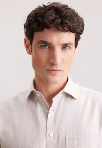 Jasnokremowa koszula zapinana na guziki z wzorem w jodełkę, z kołnierzykiem w szpic i kieszonką na piersi. Gładka tekstura materiału.