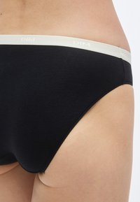 Μαύρα βαμβακερά εσώρουχα με μαλακή, ελαστική μέση που φέρει το κείμενο "DIM" σε ανοιχτό χρώμα. Λείος υφή και εφαρμοστή γραμμή.