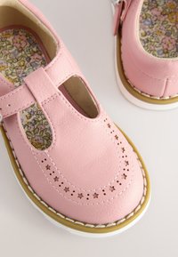 Chaussures en cuir rose clair avec un bout arrondi, motif d'étoiles découpées, semelle blanche, dotées d'une bride sur le cou-de-pied et d'une doublure florale.