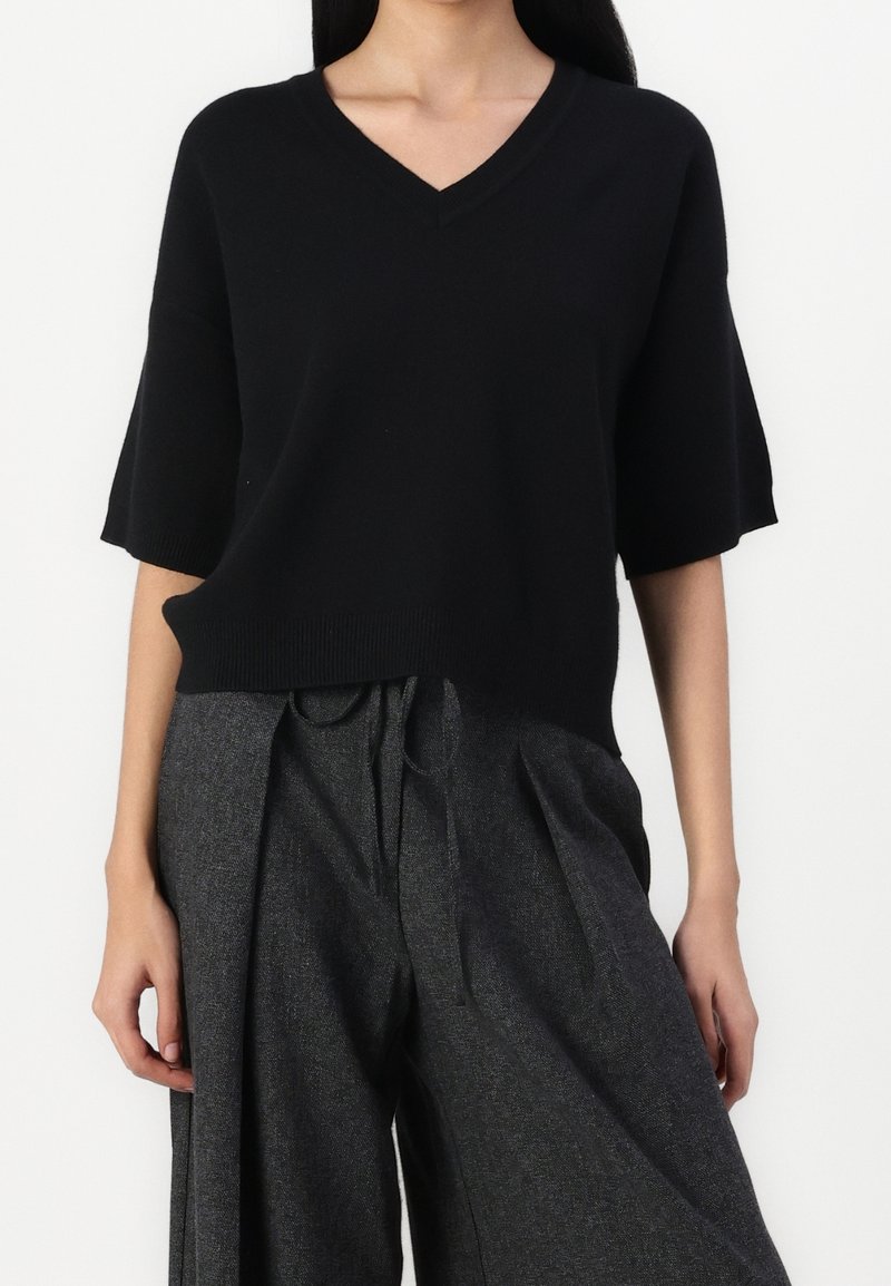 Jersey negro de manga corta y escote en V con un ajuste relajado, combinado con unos pantalones grises de cintura alta y pernera ancha con detalle de lazo en la parte frontal.