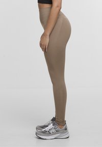 Leggings beige de cintura alta hechos de un tejido elástico, con una textura suave y detalles en las costuras, combinados con zapatillas deportivas grises.
