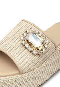 Sandali a infradito in paglia intrecciata color beige con una spessa piattaforma, caratterizzati da un grande cristallo rettangolare circondato da gemme più piccole.
