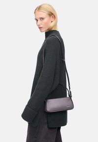 Lila Leder-Crossbody-Tasche mit sleekem Design, verstellbarem Riemen und dezenten Hardware-Details, kombiniert mit einem dunkelgrünen Strickpullover.