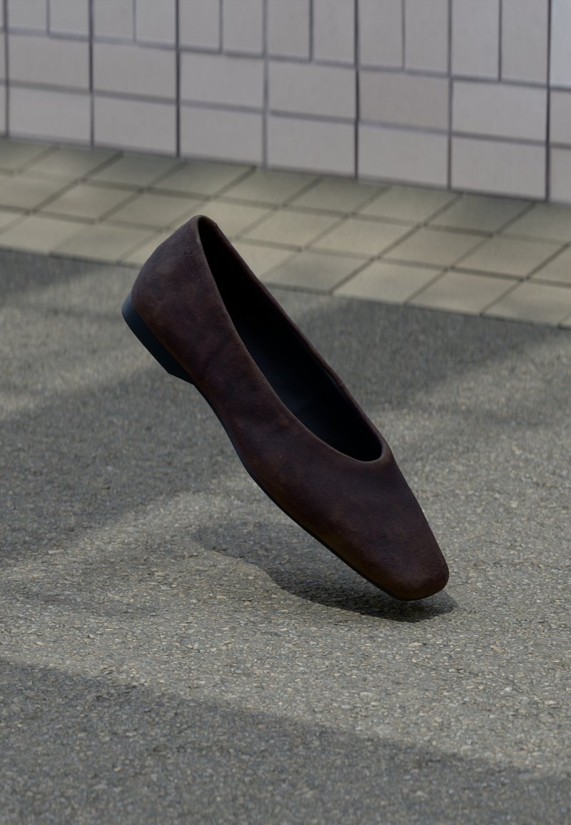 Ενιαίο σκούρο καφέ επίπεδο παπούτσι να επιπλέει πάνω από υφή έδαφος με φόντο τοίχο από πλακάκια.