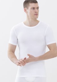 Camicia bianca a maniche corte, scollatura rotonda, realizzata in tessuto liscio. Si adatta aderente al corpo, con cuciture minime, esaltando una silhouette slanciata.