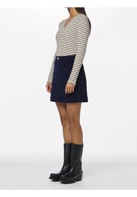 Randig, ribbad långärmad topp i kräm- och marinblå, parat med en marinblå corduroykjol med framknäppning och fickor. Svarta ankelstövlar.