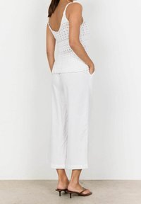 Biały dzianinowy top na ramiączkach z regulowanymi paskami, w połączeniu z luźnymi białymi spodniami z lnu i brązowymi sandałami na obcasie. Teksturowany i lekki design.
