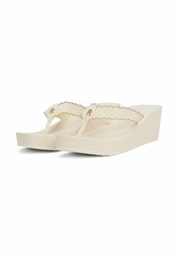 Chanclas de cuña en blanco roto con una correa texturizada que presenta un borde ondulado y un acento en logo dorado, con una suela lisa y ligeramente curvada.