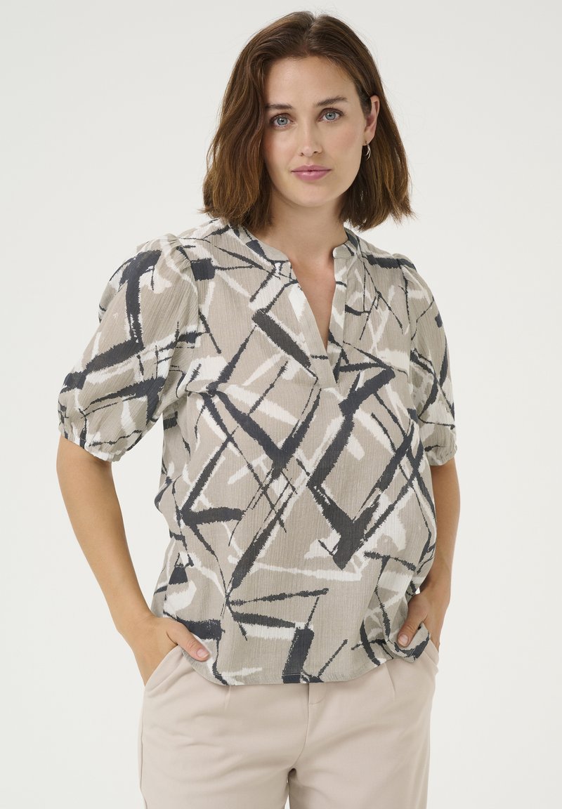 Lichtgewicht, neutraal gekleurde blouse met geometrisch zwart-wit patroon, korte pofmouwen en een V-halslijn. Heeft een relaxed fit.