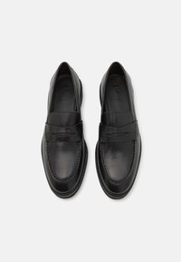 Sorte lærloafers med en sømmet design og flate såler. Oversiden har et dekorativt belte og en glatt tekstur.