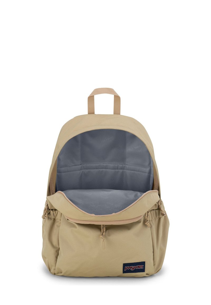 Sac à dos beige avec un grand intérieur gris, en tissu doux, straps réglables et une poche frontale zippée. Présente une étiquette de logo sur le côté.
