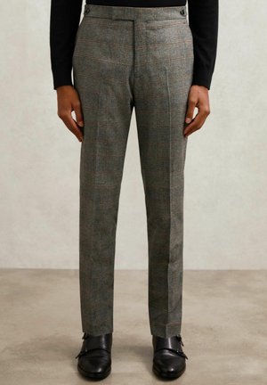 Szürke kockás nadrág, amely testre szabott fazonnal rendelkezik, texturált anyagból készült, finom narancs és kék vonalakkal, fekete cipővel párosítva.