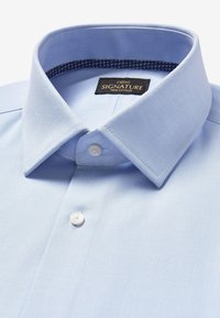 Camicia in cotone azzurro chiaro con colletto strutturato, due bottoni bianchi e dettaglio decorato all'interno del colletto. L'etichetta riporta "next SIGNATURE 100% COTTON."