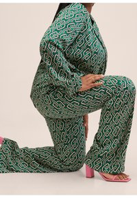 Pantalon-pantalon vert et blanc à motifs avec un design en chaîne, doté d'un tissu brillant, de pantalons évasés et de sandales à talons blocs roses.