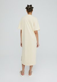 Beige, knie-lange jurk met korte mouwen, een comfortabele pasvorm, zijsplitsen en een soepele katoenen stof. Minimalistisch ontwerp zonder patronen.