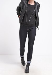 Svart läderbomberjacka över en svart topp, parat med mörk denimjeans och svarta ankelstövlar. Jeansens fållar är uppkavlade.